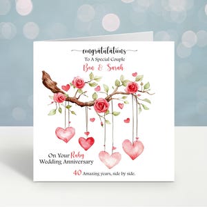 May include: A white card with the text "congratulations" and "To A Special Couple Ben & Sarah". It features a watercolour illustration of a branch with roses and hanging hearts. The text reads "On Your Ruby Wedding Anniversary 40 Amazing years, side by side."