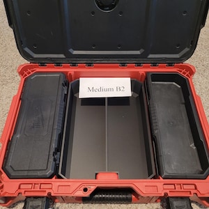 May include: Open red and black tool case with multiple compartments. The case has a black handle and latches. The text "Medium B2" is on a white label inside the case. The case is designed to hold tools and accessories.