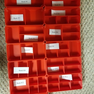 May include: Thirteen red plastic storage containers with dividers. Each container is labeled with a number from R1 to R13.