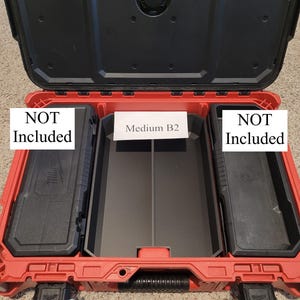 May include: Open red and black tool case with the lid open. The case has a black handle and two black storage containers on either side. The center section has a black tray with the text "Medium B2". The text "NOT Included" is on the left and right.