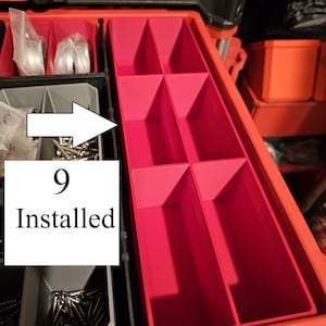 May include: A red toolbox organizer with multiple compartments. The organizer has a series of red dividers creating various storage spaces. The text "9 Installed" is visible on a white label. The toolbox is open, revealing its contents.