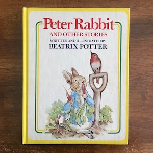 May include: A yellow book cover with the title "Peter Rabbit and Other Stories" written in black. The book is illustrated with a rabbit eating a carrot and a robin perched on a shovel.