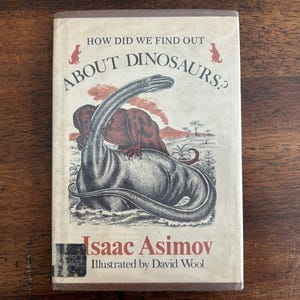 May include: A hardcover book titled How Did We Find Out About Dinosaurs? by Isaac Asimov, illustrated by David Wool. The off-white cover features a detailed black and white illustration of a long-necked dinosaur in water with a red volcanic background.