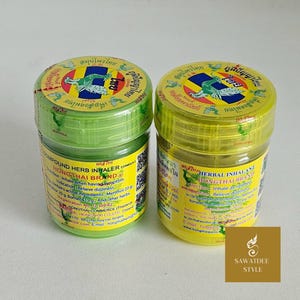 May include: Two small, round, green and yellow jars of Hongthai Brand Compound Herb Inhaler. The jars have a screw-on lid and a label with text in Thai and English. The labels feature a green crocodile illustration and the text "HONGTHAI BRAND".
