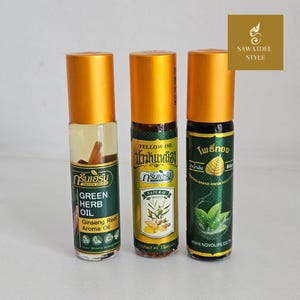 May include: Three cylindrical glass roll-on bottles with gold caps. The left bottle contains clear oil with a visible ginseng root. The middle bottle has a yellow label with ginger illustrations. The right bottle features a green label with a leaf graphic.