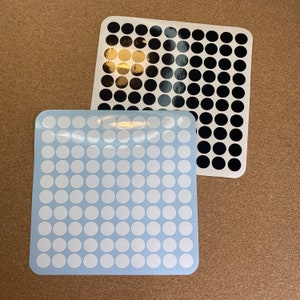 Op de afbeelding: Drie vellen ronde stickers. Eén vel heeft witte stickers op een lichtblauwe achtergrond. Een ander vel heeft zwarte stickers. Het derde vel heeft gouden stickers. De stickers zijn in een rasterpatroon gerangschikt.