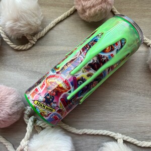 Puede incluir: Un vaso verde y blanco con un diseño de slime que gotea. El vaso presenta una variedad de personajes de dibujos animados y el texto "Adam Bomb".