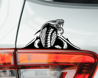 May include: Black and white vinyl sticker of a cobra snake with its hood raised, applied to the back of a silver car.