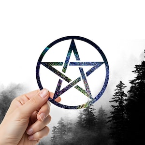 May include: A circular pentagram with a glittery, multicolored design held in front of a misty forest backdrop. The star is outlined in dark blue and has a five-pointed star shape.