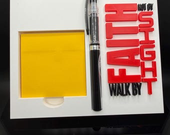 Puede incluir: Un organizador de escritorio blanco con un bloc de notas adhesivas amarillo y un bolígrafo negro. Las palabras "NOT BY SIGHT, WALK BY FAITH" están en letras 3D rojas.
