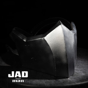 Puede incluir: Una máscara facial negra y plateada con un diseño geométrico. La máscara tiene una forma afilada y angular y está hecha de un material duro. La máscara es un accesorio popular para cosplay y Halloween.