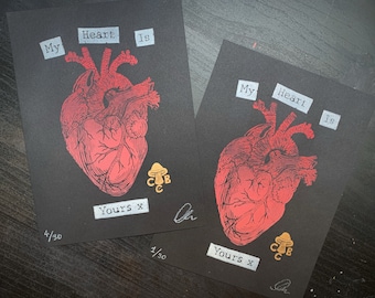 Könnte beinhalten: Zwei Schwarzweißdrucke eines roten anatomischen Herzens mit dem Text "My Heart Is" und "Yours x" auf jedem Druck. Die Drucke sind mit 4/30 und 1/30 nummeriert. Jeder Druck zeigt auch eine kleine goldene Pilzgrafik mit den Buchstaben "CUB" darauf.