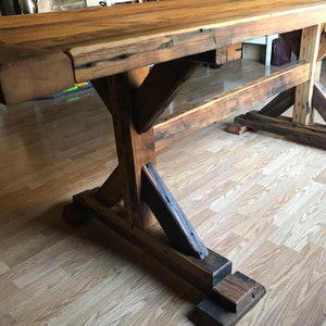 May include: A rustic wooden table with a thick, weathered top and a sturdy, X-shaped base. The table is made from reclaimed wood and has a natural, distressed finish.