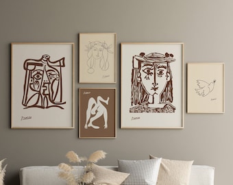 May include: Five framed brown line drawings of figures and a dove by Pablo Picasso, hanging on a beige wall above a white couch with pillows and a woven coffee table.