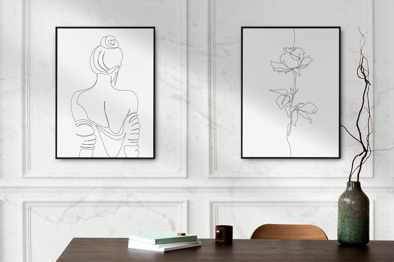 May include: Two black framed prints on a white wall. The print on the left is a line drawing of a woman's back. The print on the right is a line drawing of a single rose.
