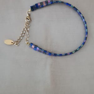 Peut inclure: Un bracelet bleu et iridescent avec un fermoir doré. Le bracelet est composé de petites perles carrées.