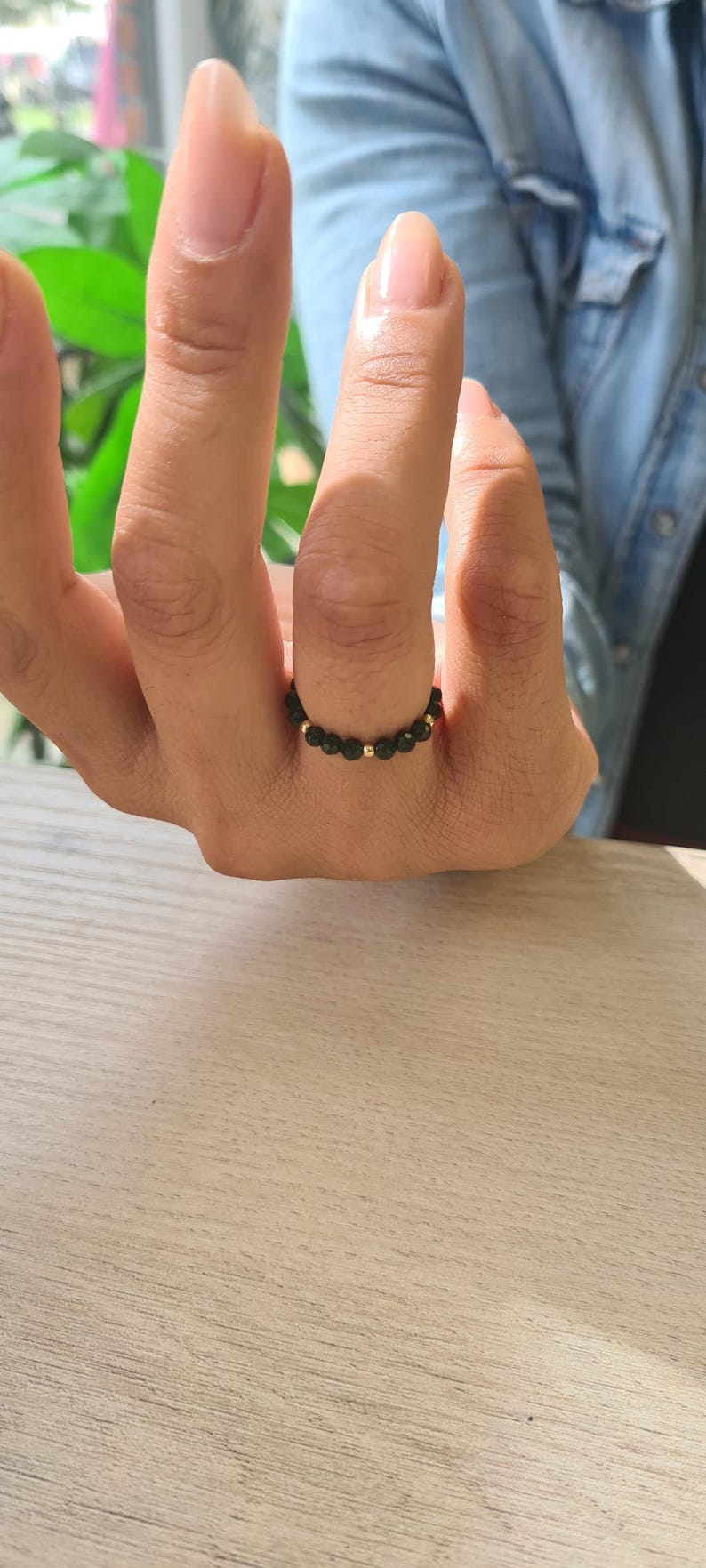 May include: A black beaded ring with gold-coloured accents. The ring is made of small, round black beads and interspersed with gold-coloured beads. The ring is on a finger.
