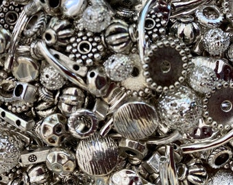 May include: A large assortment of silver-toned metal beads and charms. The beads are of various shapes and sizes, including round, square, and oval. Some of the beads have intricate designs, while others are plain.