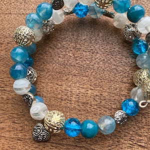 Könnte beinhalten: Ein blaues und weißes Perlenarmband mit silbernen und goldenen Akzenten. Das Armband hat einen herzförmigen Anhänger.