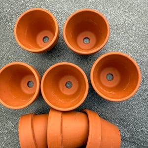 Könnte beinhalten: Sieben Terrakotta-Blumentöpfe in verschiedenen Größen. Die Töpfe sind unglasiert und haben eine natürliche braune Farbe. Einige der Töpfe sind übereinander gestapelt.