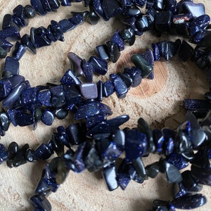 Könnte beinhalten: Eine Strähne dunkelblauer Edelsteinsplitter mit einer funkelnden, glitzernden Textur. Die Splitter sind unregelmäßig in Form und Größe und zu einer Halskette oder einem Armband zusammengefügt.