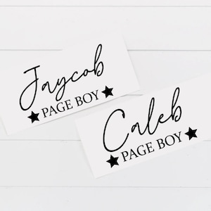 May include: Two white cards with black text. The top card says "Jaycob Page Boy" with a star on either side of the text. The bottom card says "Caleb Page Boy" with a star on either side of the text.
