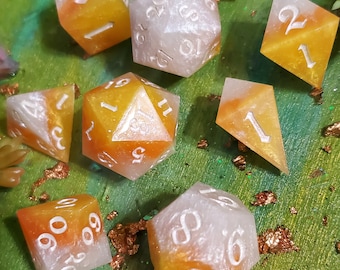 May include: A set of eight dice with a white and orange swirl pattern. The dice are numbered 1 through 6 and are made of a translucent material.