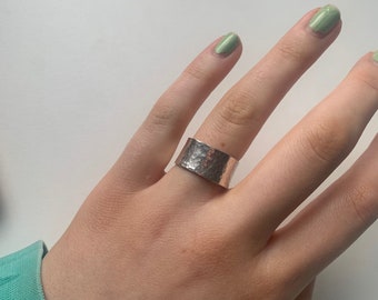 May include: A silver hammered wide band ring on a hand with green nail polish.