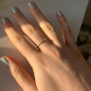 Pu&ograve; includere: Primo piano di una mano con un sottile anello a fascia d'oro. Le unghie sono dipinte di un colore blu chiaro.