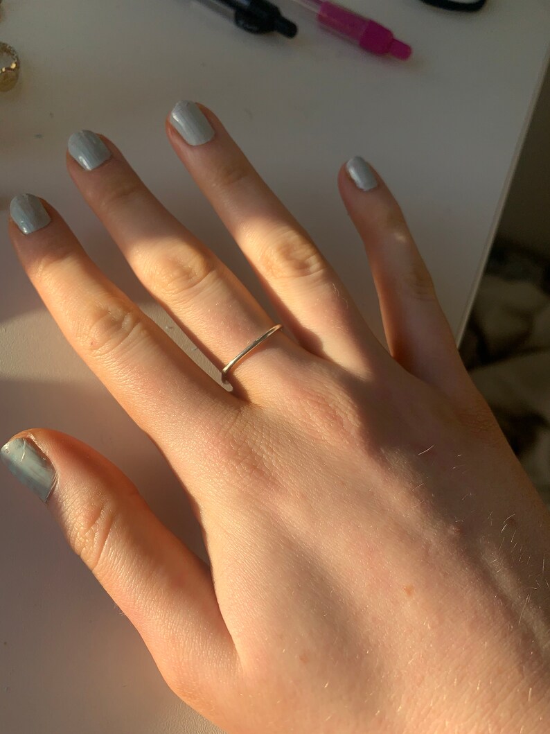 Pu&ograve; includere: Primo piano di una mano con un sottile anello a fascia d'oro. Le unghie sono dipinte di un colore blu chiaro.