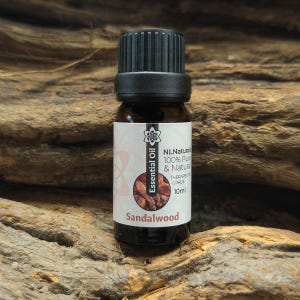 Op de afbeelding: Een kleine bruine glazen fles sandelhout etherische olie met een zwarte dop. Het etiket luidt "NL Naturals 100% Pure & Natural Therapeutic Grade" en "Sandalwood". De fles bevat 10 ml olie.