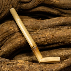 Könnte beinhalten: Eine hellbraune Bambus-Pfeife mit gebogenem Schaft. Die Pfeife liegt auf einem Haufen brauner Baumwurzeln.