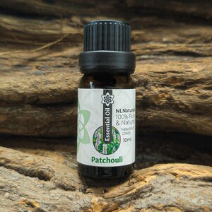May include: A small brown glass bottle of patchouli essential oil with a black cap. The label reads "NL Naturals 100% Pure & Natural Therapeutic Grade 10ml". The background is a textured wooden surface.