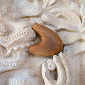Peut inclure: Un objet en bois incurvé, de couleur marron clair, se détachant sur un fond texturé blanc cassé. Le design est lisse et ergonomique, peut-être une poignée ou un élément décoratif. Le contraste suggère une esthétique naturelle.