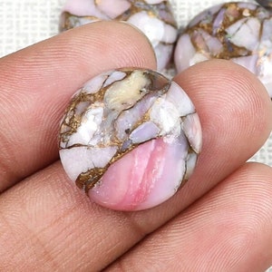 May include: A round, pink, white and gold opal cabochon gemstone with a unique, marbled pattern. The gemstone is approximately 2.5 cm in diameter.