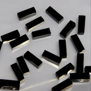 May include: A collection of black rectangular gemstone beads. The beads are smooth and polished, with a slight shine.