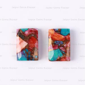 May include: Two rectangular cabochons of colourful, multi-faceted, polished stone. The stones are a mix of red, orange, pink, blue, green, and gold. The stones are set against a white background.
