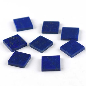 Peut inclure: Huit pierres précieuses de lapis-lazuli de forme carrée avec des paillettes dorées. Les pierres précieuses sont d'un bleu profond et sont disposées en cercle sur un fond blanc.
