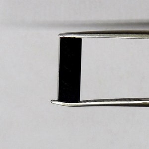 Può includere: Un oggetto rettangolare nero è tenuto da una pinzetta d'argento.