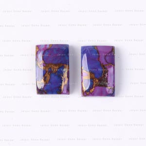 May include: Two rectangular gemstones with a vibrant mix of purple, blue, and gold colors. The stones have a polished, glossy finish, and the gold veining creates a unique pattern. The gemstones are likely for jewelry making.