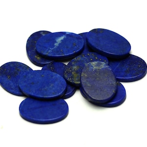 Puede incluir: Un grupo de piedras de lapislázuli de forma ovalada, cada una con un color azul intenso y motas de pirita dorada. Las piedras son lisas y pulidas, y están dispuestas en una pila sobre un fondo blanco.