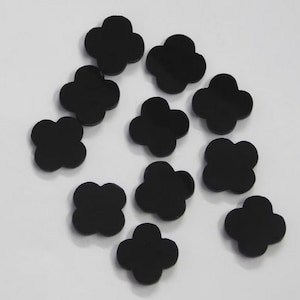 May include: Ten black clover-shaped cabochons, each with four rounded lobes, scattered on a white surface.