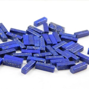 Op de afbeelding: Een verzameling kleine, rechthoekige lapis lazuli edelsteen kralen. De kralen zijn diepblauw van kleur met vlekken van gouden pyriet.
