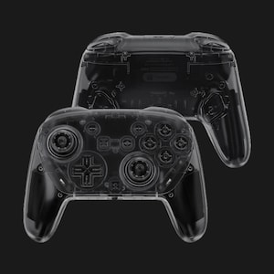 May include: Two transparent game controllers are displayed against a black background. The controllers have a clear plastic shell, revealing the internal components. The design includes buttons, joysticks, and a directional pad, typical of modern game controllers.