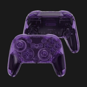 May include: Two transparent purple game controllers are displayed against a black background. The controllers have a clear, see-through design, showcasing the internal components. The buttons and joysticks are visible, and the overall aesthetic is modern and sleek.