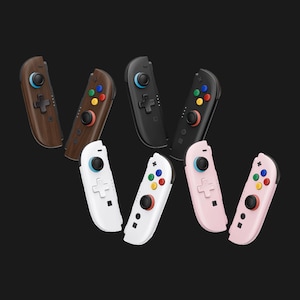 May include: A collection of eight game controllers arranged in pairs, featuring wood grain, black, white, and light pink finishes. Each controller includes a black joystick with a blue ring, a directional pad, and four colored action buttons.