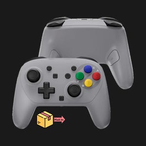 May include: Two gray game controllers are displayed against a black background. The front controller has colored buttons: blue, green, red, and yellow. The text "Mail In" is next to a box graphic.