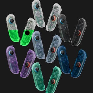 May include: A collection of twelve game controller attachments in various translucent colors including clear, black, purple, blue, and green. Each controller features a black joystick with a colored ring, directional buttons, and internal circuitry visible.