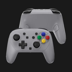 May include: Two gray game controllers are displayed against a black background. The controllers have black joysticks, buttons, and directional pads. The face buttons are colored blue, green, red, and yellow. The controllers are designed for gaming.