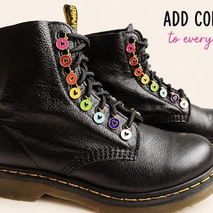 Puede incluir: Botas de cuero negro adornadas con abalorios en forma de corazón arcoíris ensartados en los cordones. Los abalorios son de varios colores. El texto "ADD COLOUR to every step" es visible. Costuras amarillas.